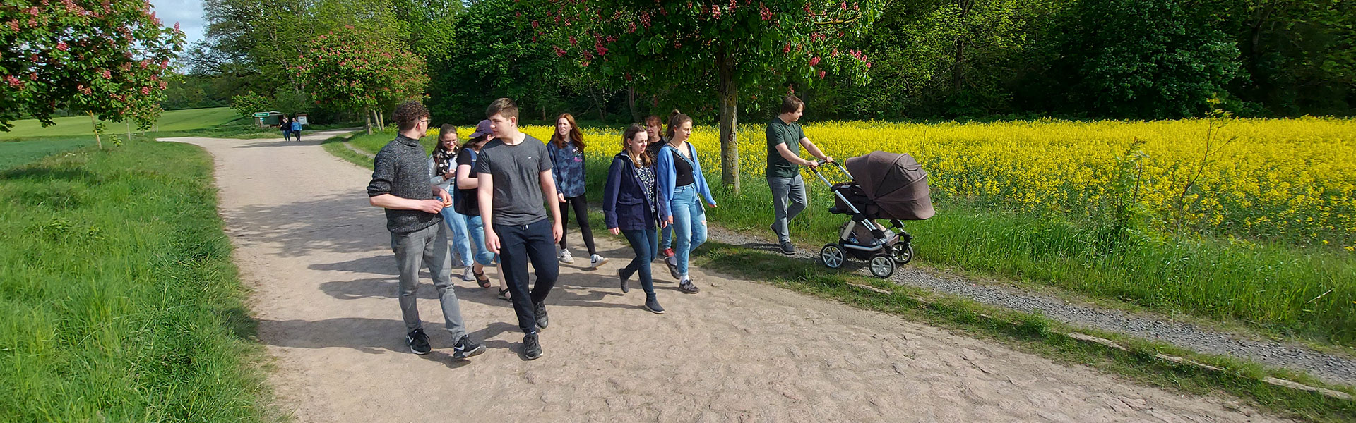 Gruppe Jugendlicher die auf einem Feldweg entlang eines Rapsfeldes geht